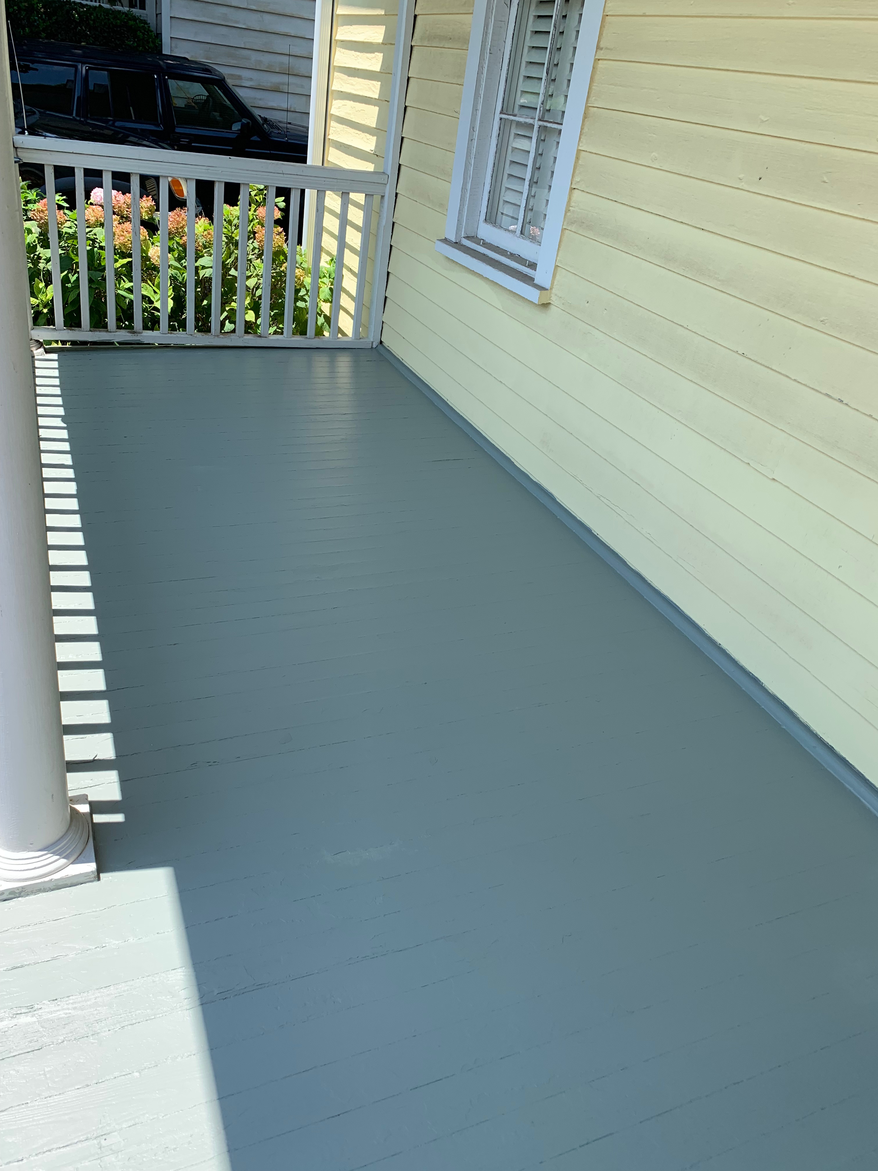Newly painted gray porch floor alongside a pale yellow house with white trim.