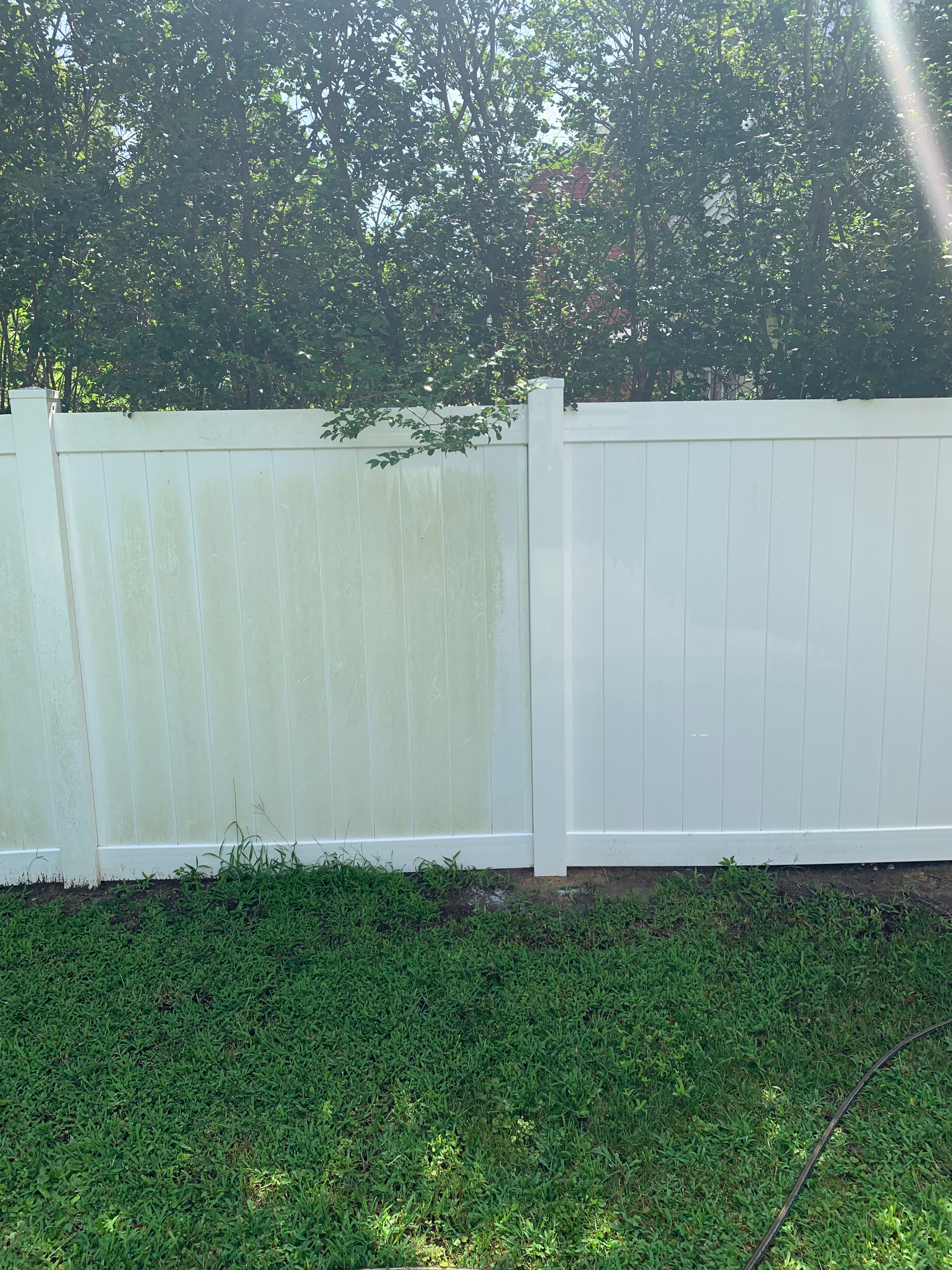 Partially pressure washed vinyl fence showing clean and dirty panels.